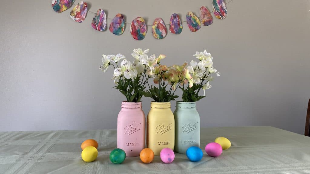 Three chalk painted mason jars with colored eggs as table centerpiece