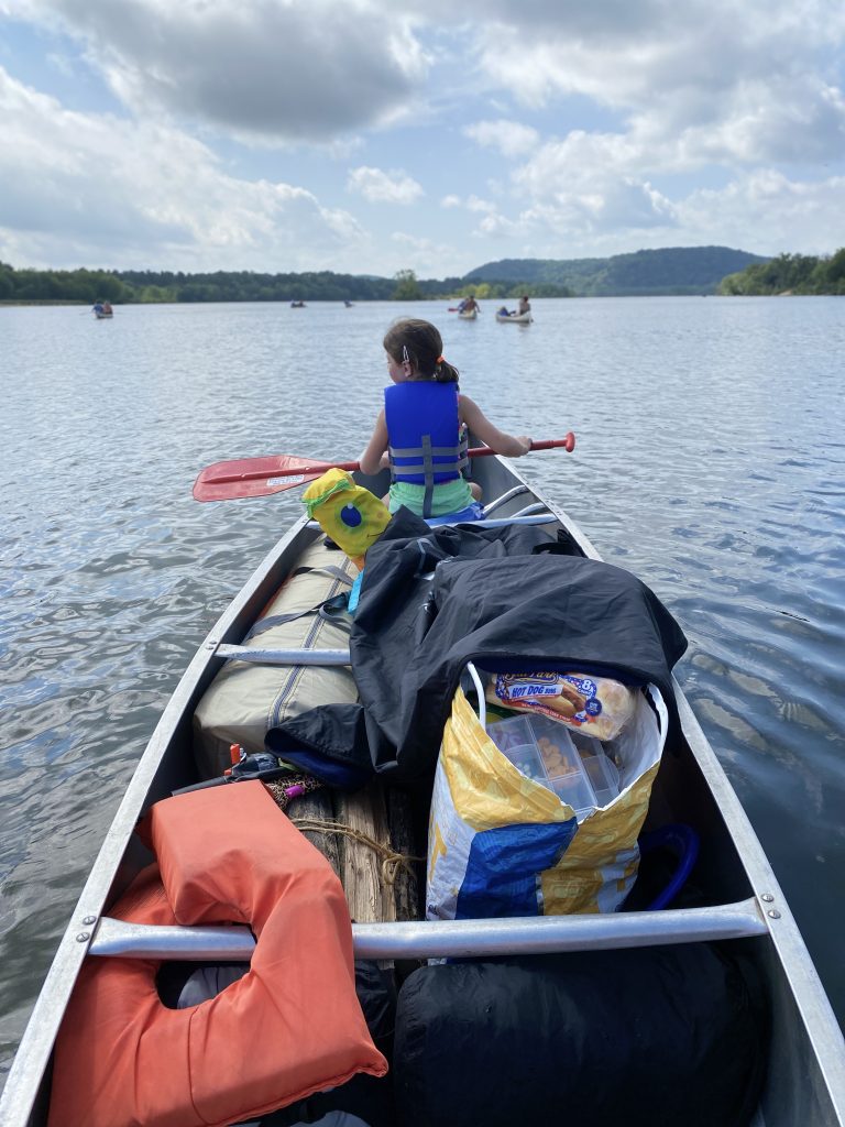 canoe filled with camping supplies and girl with paddle in life jacket