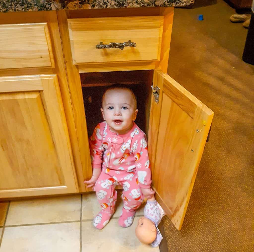 toddler sitting in a lower kitchen cabinet