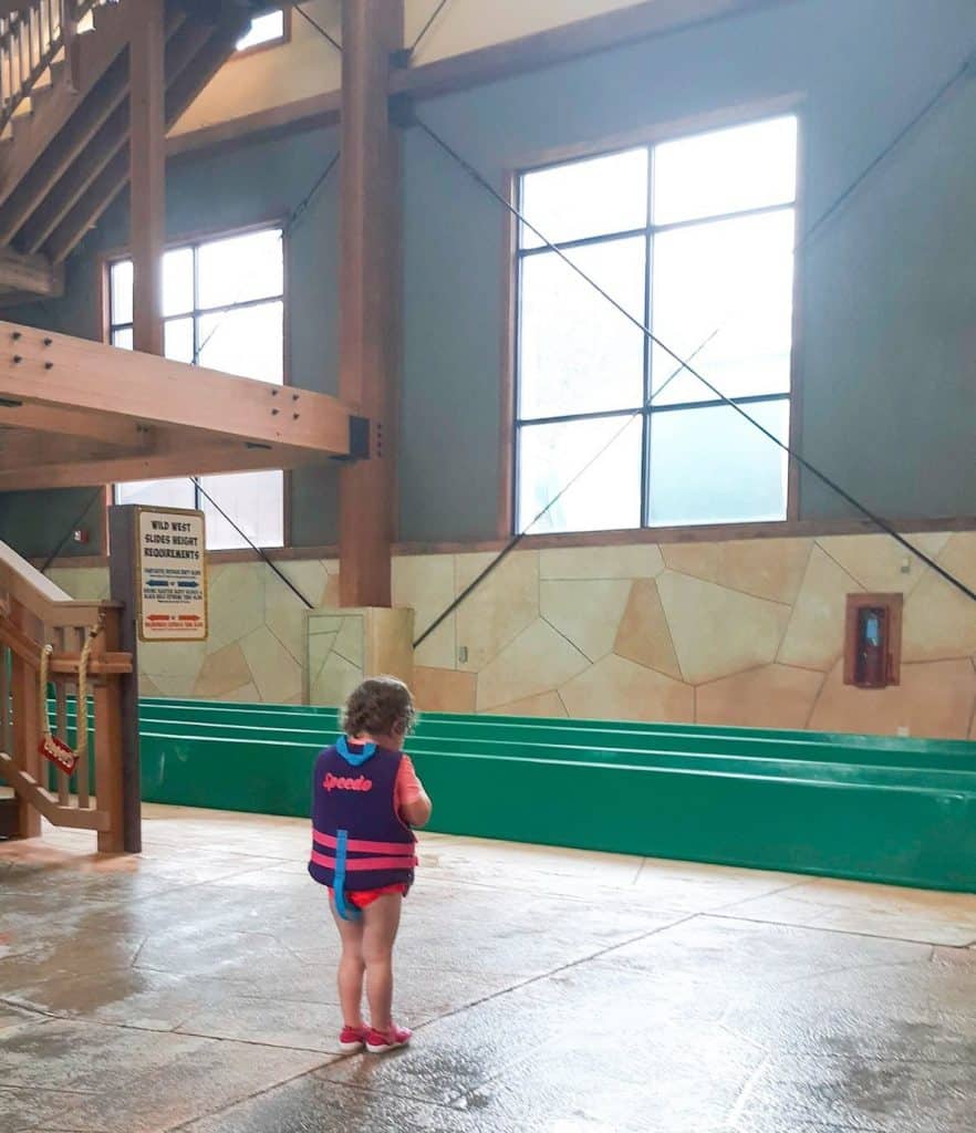 the back of a toddler in a life jacket by a indoor water slide