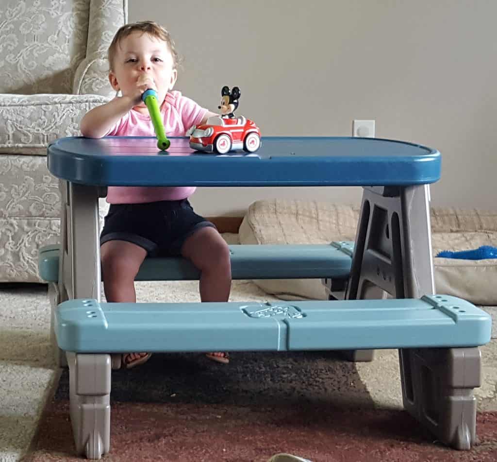 toddler sitting at child's picnic table playing the recorder