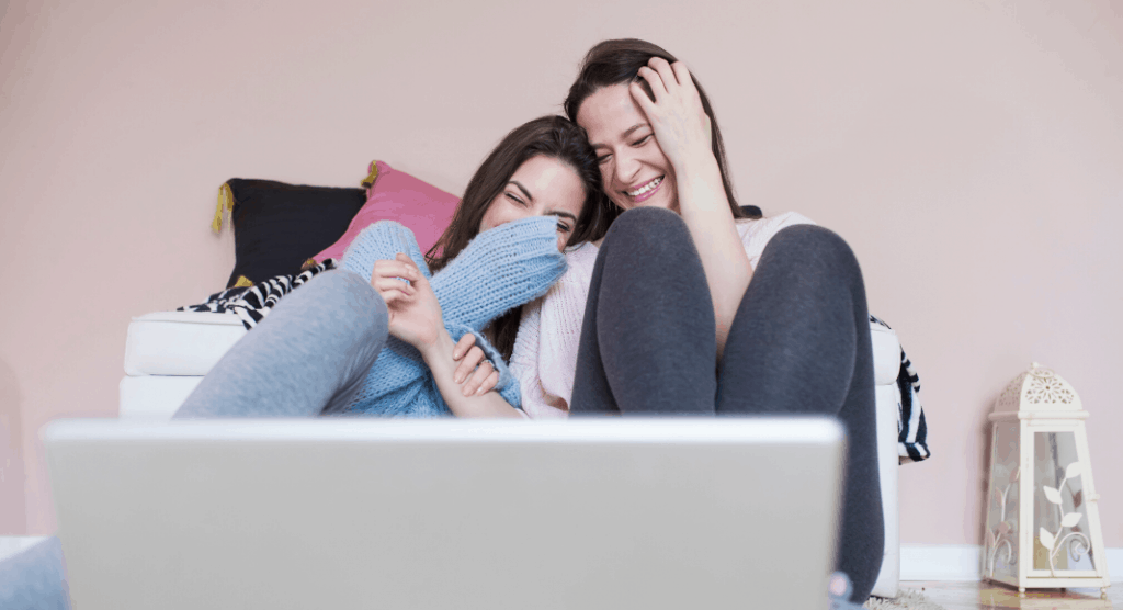 two woman laughing while looking at computer