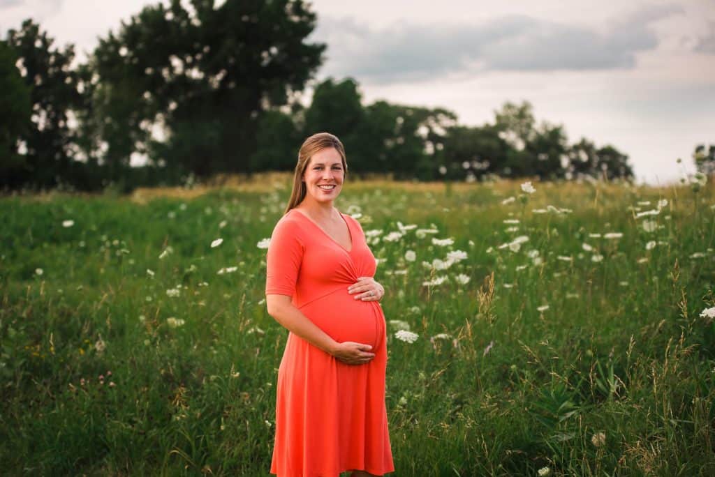 pregnant woman standing in front of a field of wildflowers